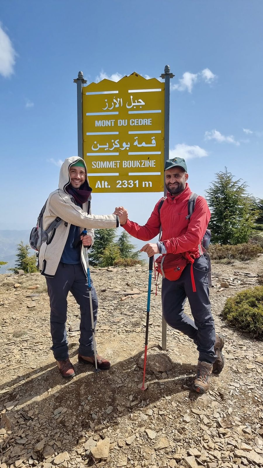 Two hikers shaking hands at the official Sommet Boukzine sign, 2331m